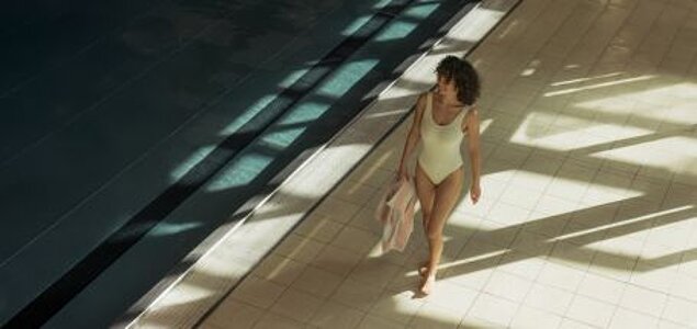 Frau im Badeanzug geht am Hallenbad entlang.