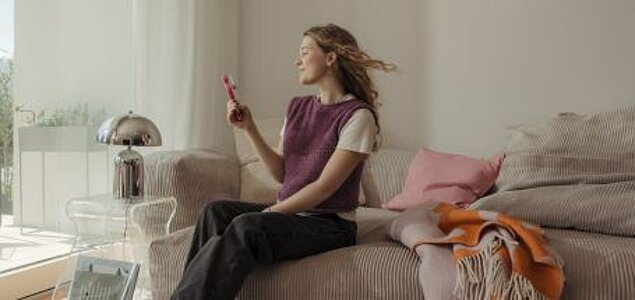 Frau kühlt sich mit Handventilator auf dem Sofa